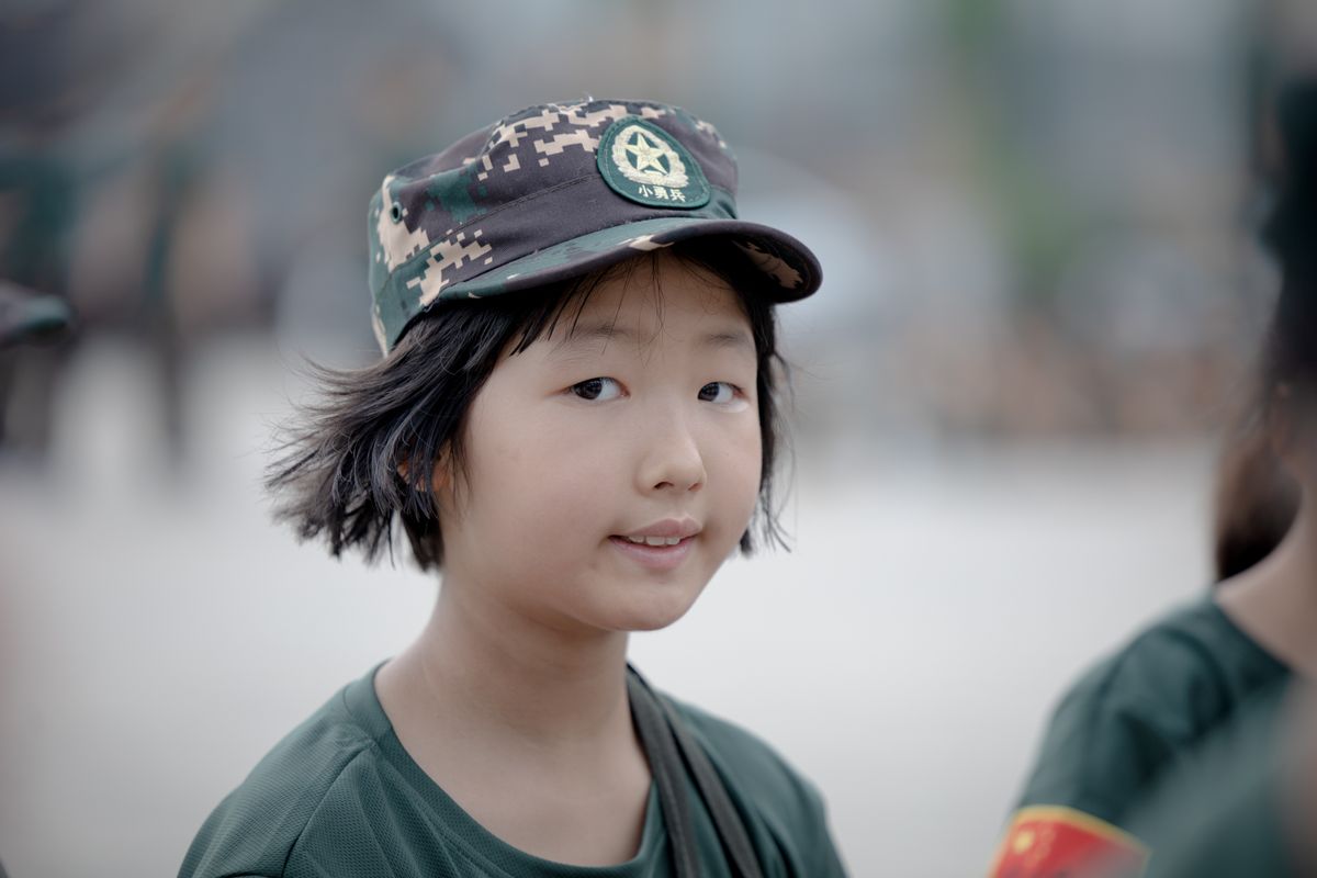 Young Asian child in scout uniform and cap during outdoor camp activity in China.