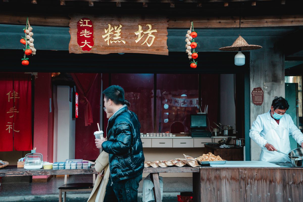 A bustling street food stall offering traditional dishes to a customer in stylish winter attire.