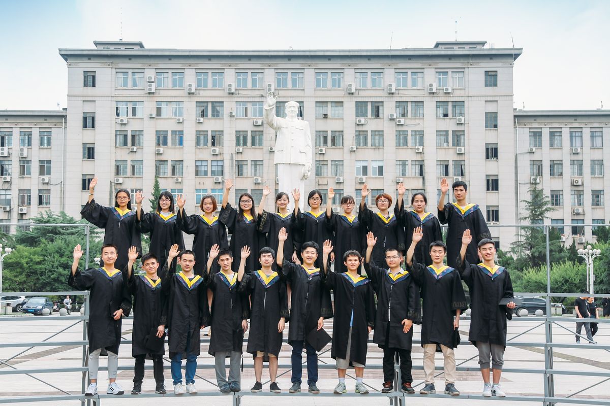 Group of graduates in gowns posing outdoors in front of university building.