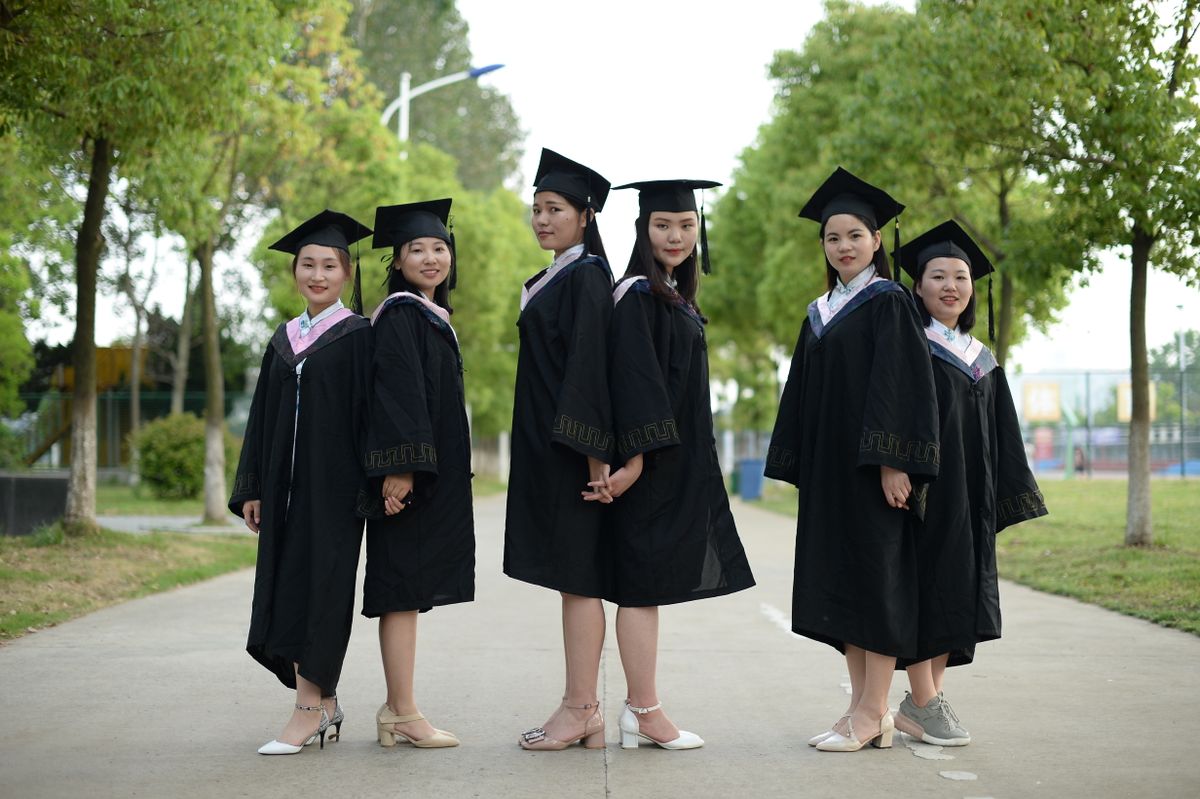 Group of five female graduates in caps and gowns posing outdoors.