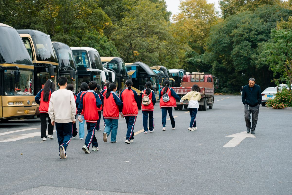 Students in sports uniforms walking towards buses in Hangzhou parking area.