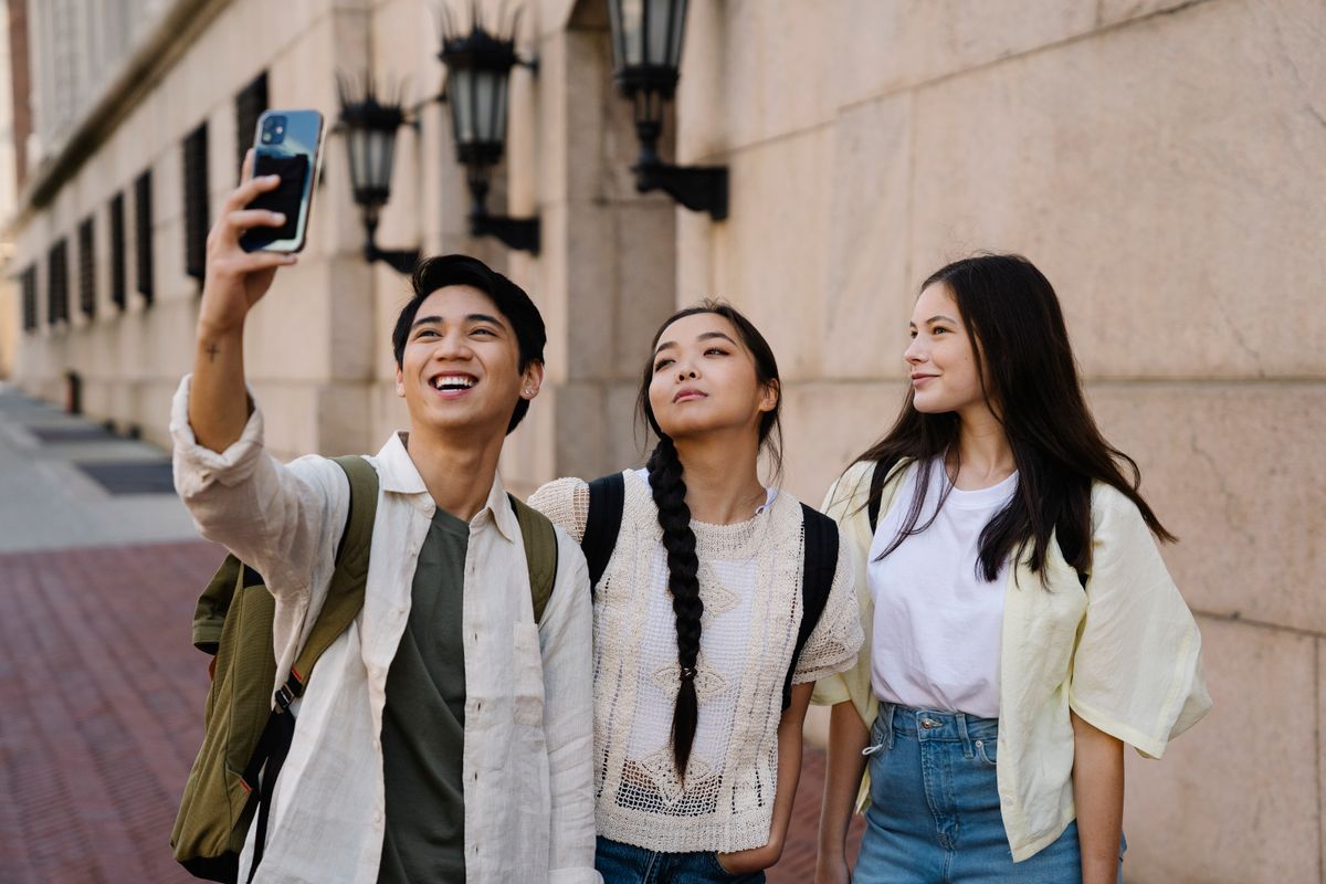 Three friends smiling and taking a selfie together on a city street.