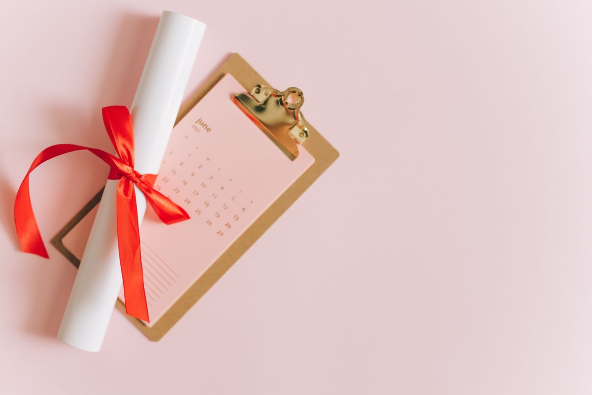 Rolled diploma with red ribbon on clipboard next to June calendar, perfect for graduation season themes.