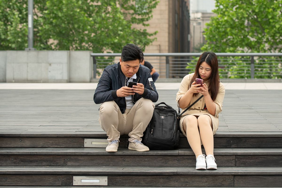 Young couple absorbed in smartphones on wooden steps in urban Shanghai.
