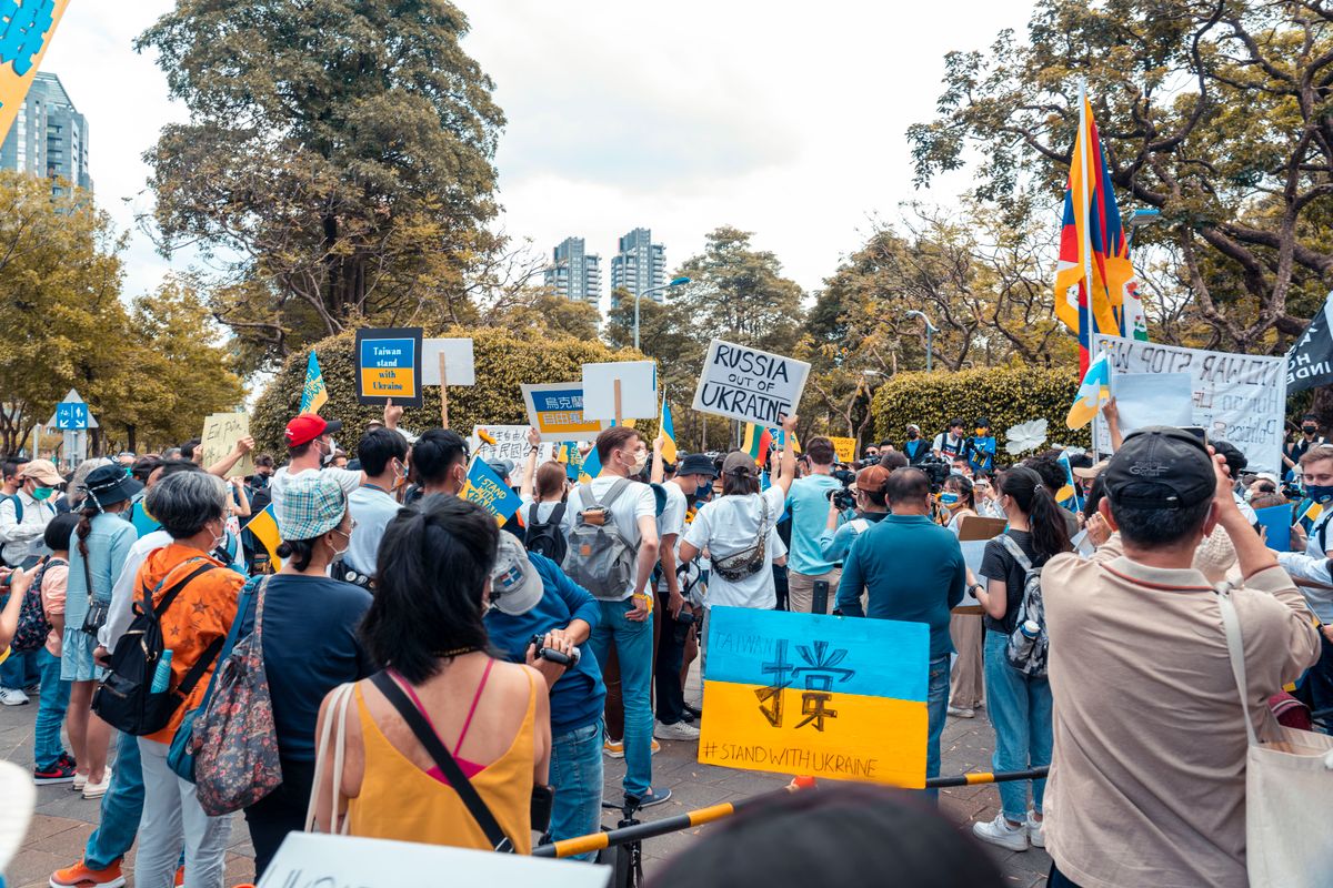 Crowd gathered outdoors showing support for Ukraine with flags and banners.