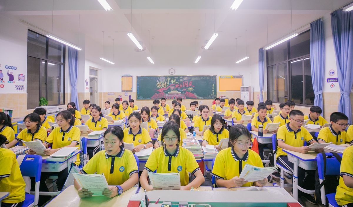 A large group of students in yellow uniforms engaged in classroom activities, reading and learning.