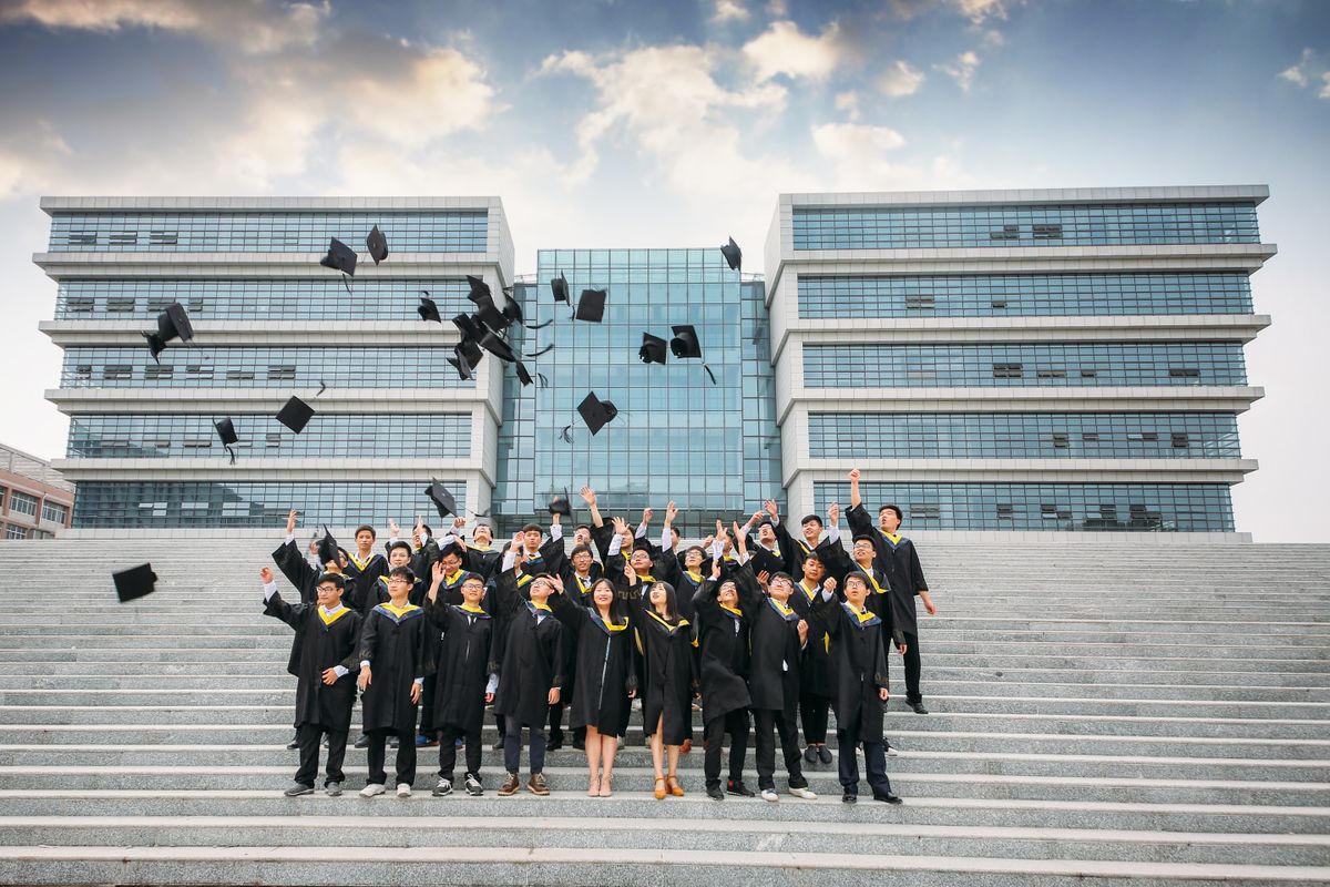 Group of graduates celebrating and tossing caps outside modern building.