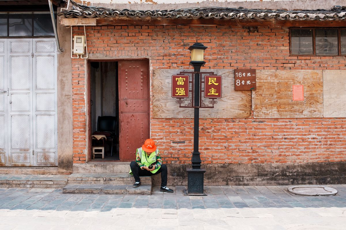 A construction worker in a reflective vest and helmet relaxing on a street during the day.