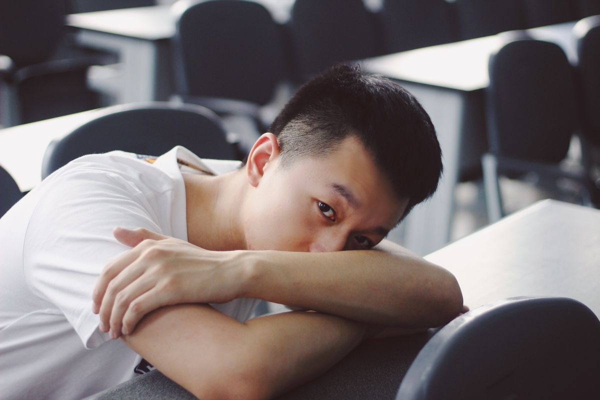 Asian man relaxing in a classroom, resting on a desk. Calm and peaceful atmosphere.