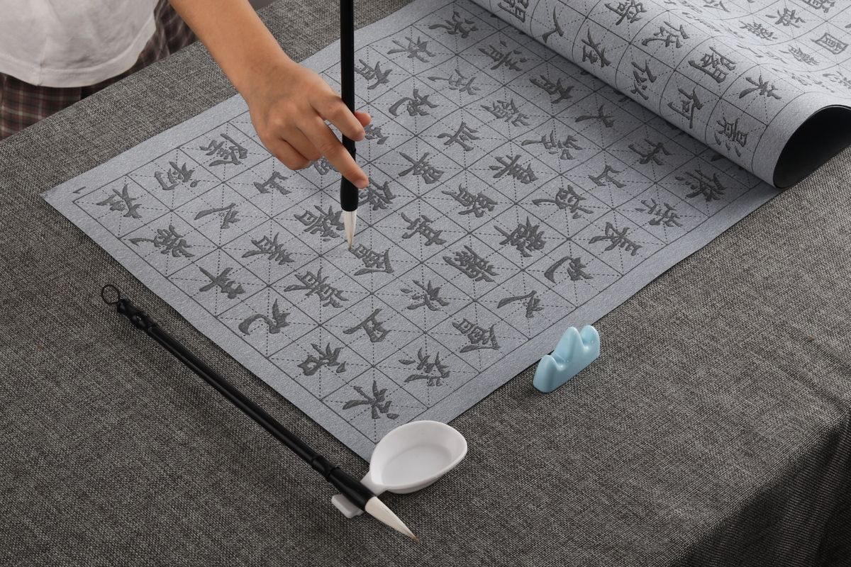 A hand demonstrates calligraphy techniques using a brush on grid paper, showcasing traditional art.