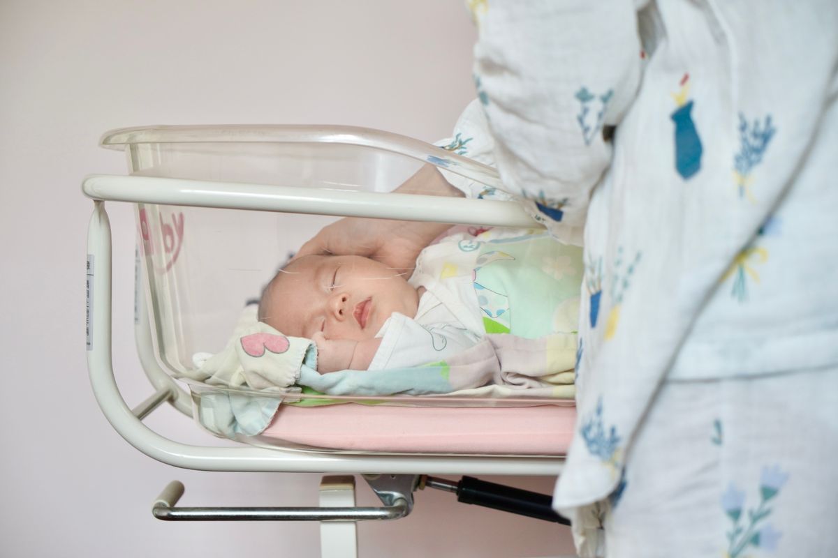 A tender moment of a newborn baby sleeping peacefully in a hospital bassinet being gently touched by a parent.