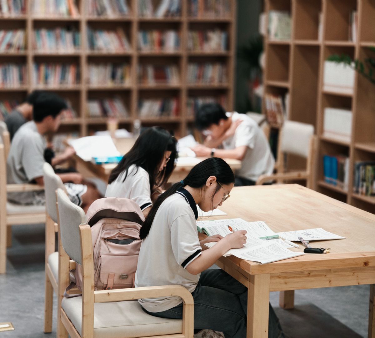 Group of students focused on studying inside a library, surrounded by bookshelves.