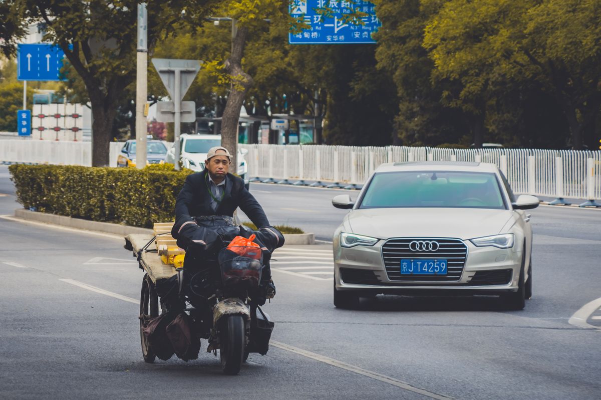 A motorbike and silver car navigate through Beijing streets in an urban traffic setting.