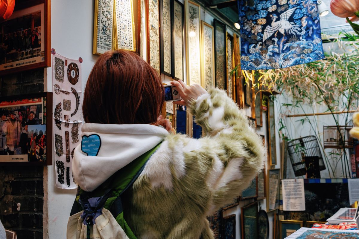 A young woman photographing framed artwork in a vibrant Beijing gallery.