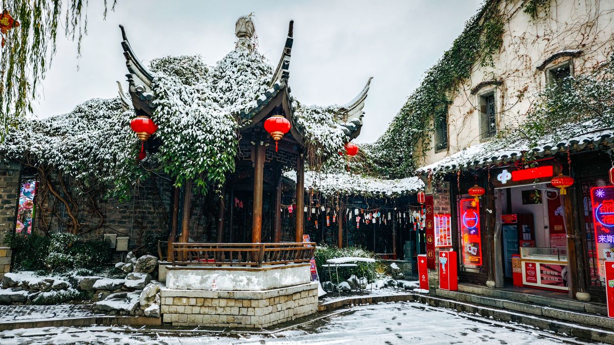 A picturesque Chinese courtyard with snow-covered traditional architecture and red lanterns, creating a serene winter atmosphere.