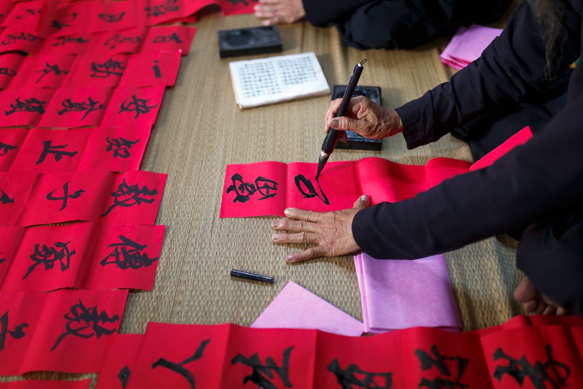 Skilled hands creating beautiful Asian calligraphy on red paper, symbolizing culture and tradition.