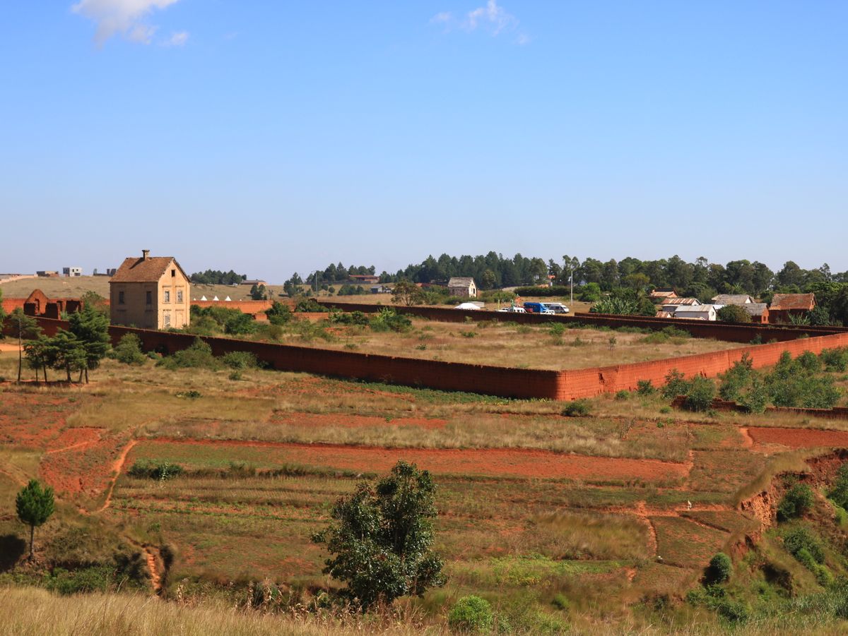 A beautiful rural scene featuring a traditional house and expansive red soil landscape under a clear blue sky.